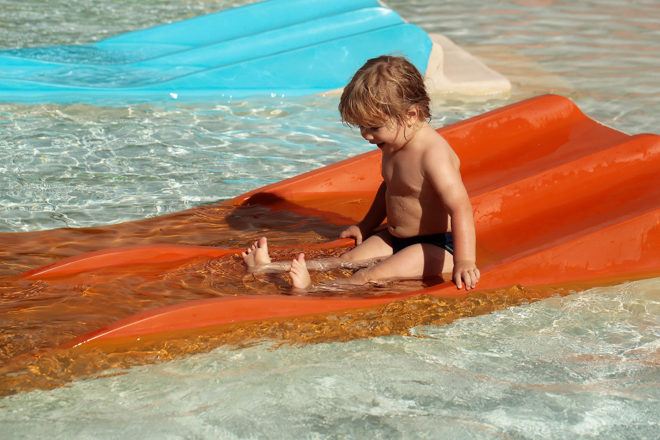 Glückliches Kind auf der orangefarbenen Wasserrutsche im Wasserpark
