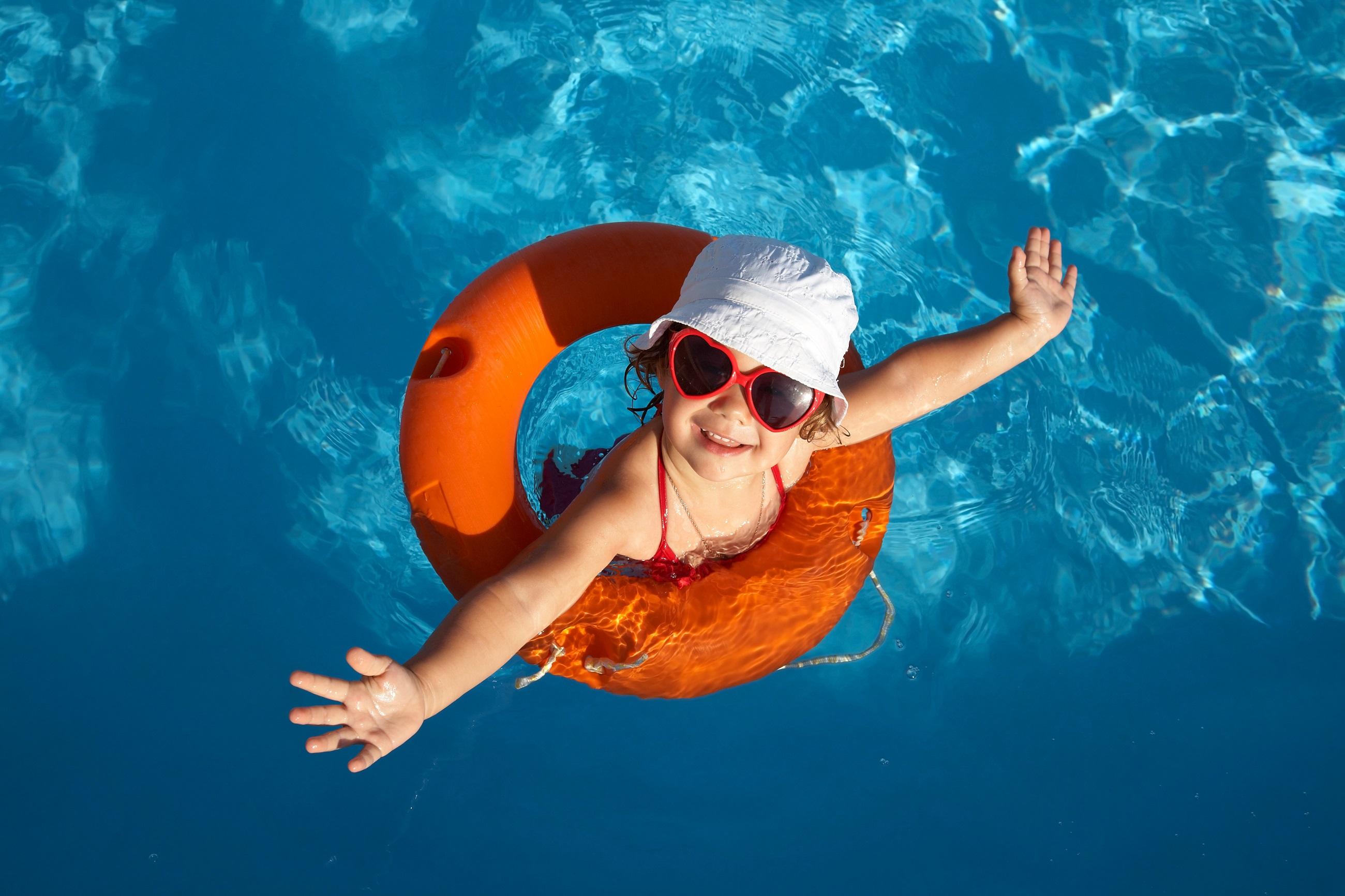 Glückliches kleines Mädchen mit roter Sonnenbrille im Wasserpark