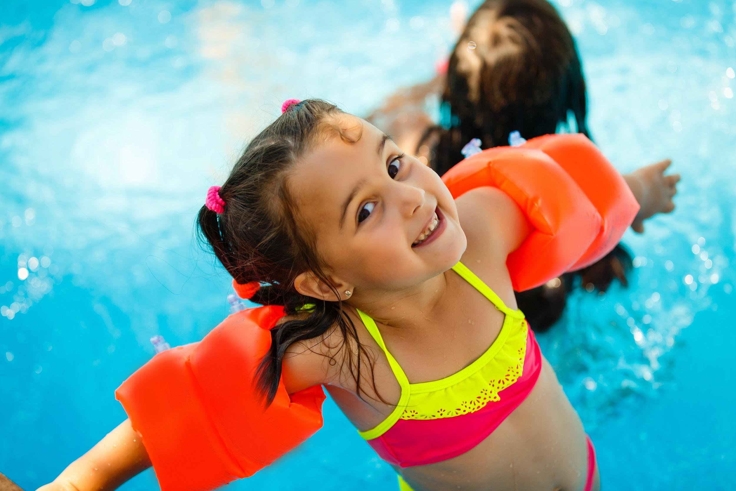 Kleines Mädchen im Wasserpark mit orangefarbenen Schwimmärmeln