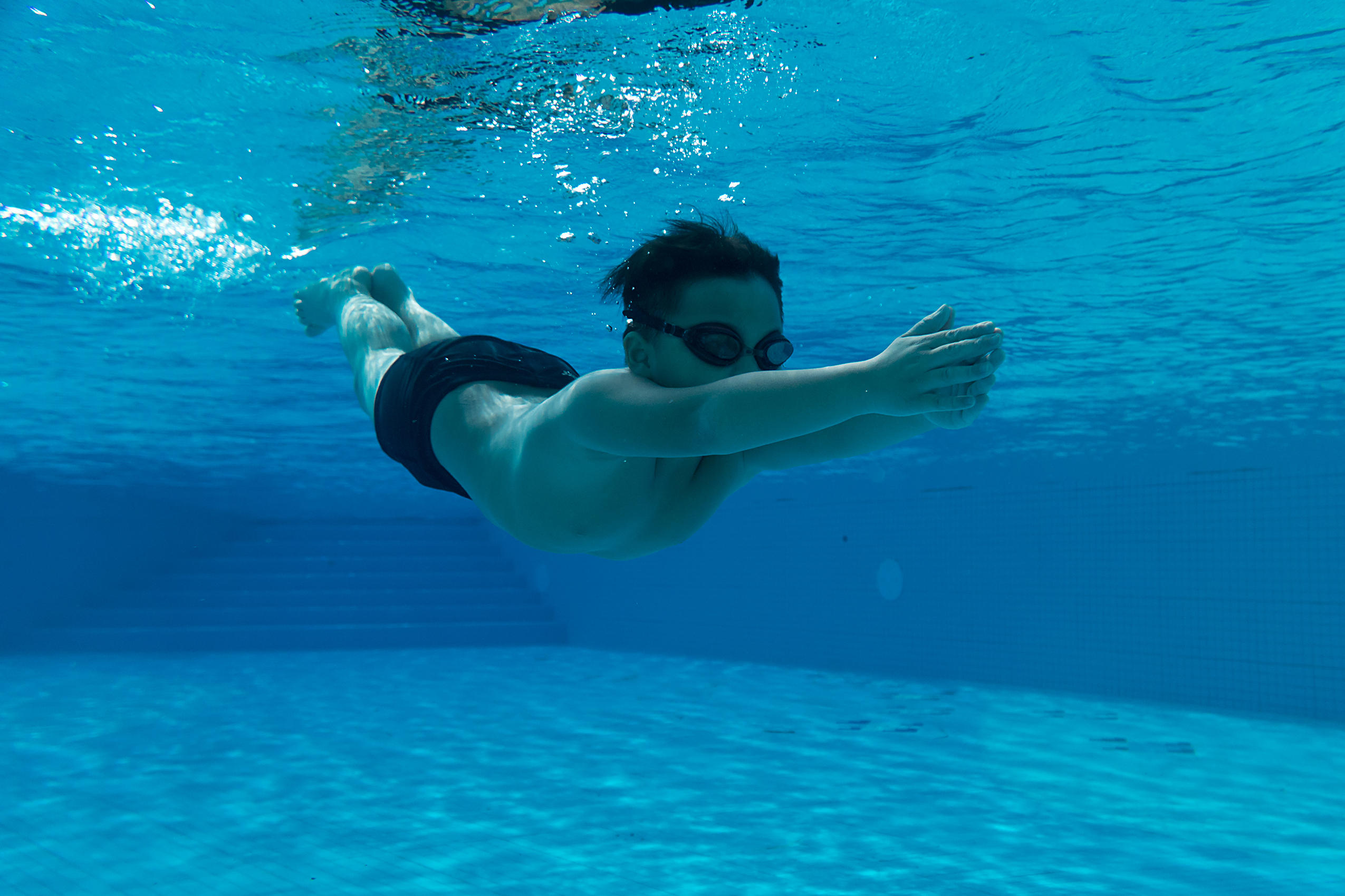 Schwimmender kleiner Junge in dunkler Hose im Wasserpark